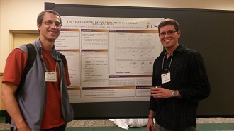 Two men standing on either side of a poster in a conference hall. The men are smiling at the camera and wearing name tags.